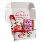 Front view of two 14 oz Kiss Me Pasta bags showing pink label and tri-color heart- and kiss-shaped pasta on white background